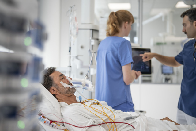 Servo-u in clinical environment with adult intubated patient, nurse and clinician discussing on screen ventilator values