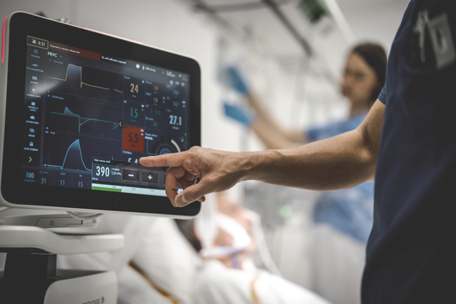 Servo-u screen in clinical environment with a hand touching the screen and an intubated patient in the background
